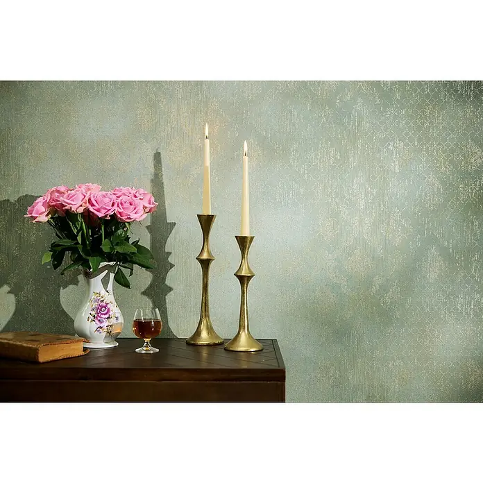 A.S. Création Metropolitan Stories Hot Spots Vliestapete - Grün-Champagner-Metallic, Ornament, 10,05 x 0,53 m - Elegantes Stillleben mit Rosen, Kerzenständern und einem Glas auf einem dunklen Holztisch vor einer gemusterten Wand.