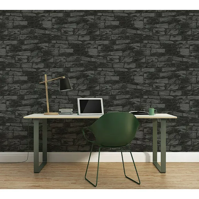 A.S. Création Vliestapete Stein - Schwarz, Steinoptik, L x B: 10,05 x 0,53 m - Ein Schreibtisch mit einem Laptop, einer Lampe und einem grünen Stuhl vor einer dunklen Steinwand-Tapete, die eine elegante Arbeitsumgebung schafft.