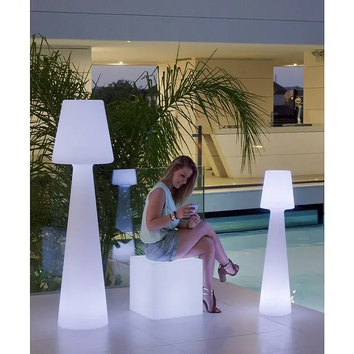 New Garden Lámpara de diseño para exterior LED Lola - 25 W, Blanco frío, Altura: 110 cm - Mujer sentada en un cubo iluminado entre dos lámparas de pie decorativas con pantallas.