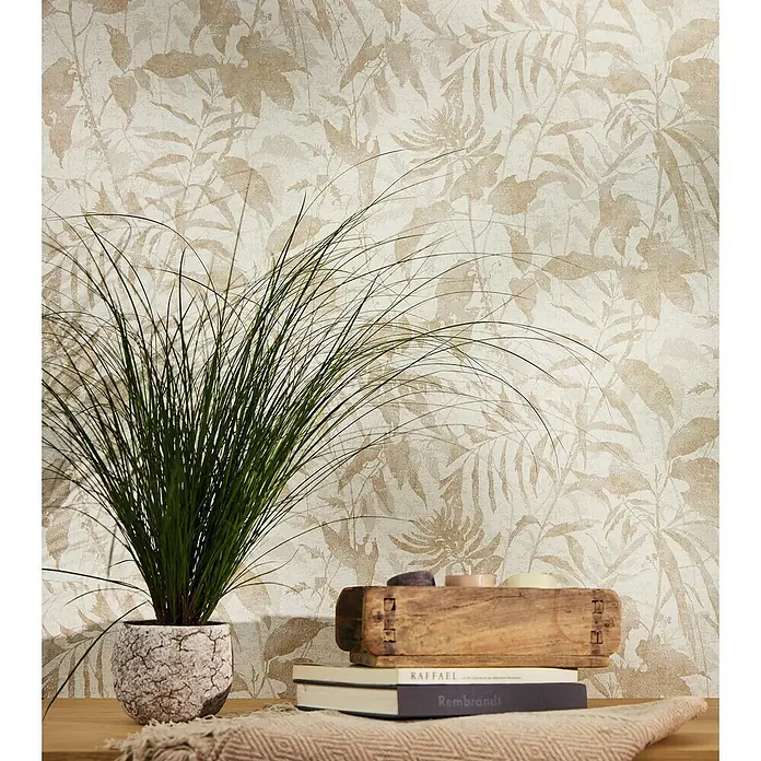 A.S. Création Metropolitan Stories Hot Spots Vliestapete Dschungel - Creme-Beige-Metallic, Floral, 10,05 x 0,53 m - Dekorative Inneneinrichtung mit einer grünen Pflanze im Topf, Büchern und einer Holzkiste auf einem Tisch vor einer floralen Tapete.