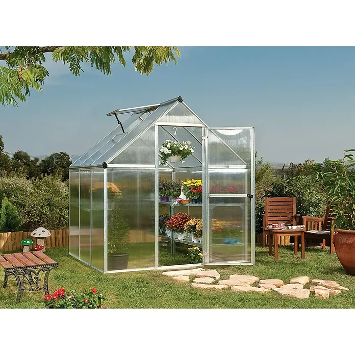 Palram – Canopia Gewächshaus Mythos 6x6 - Außenmaß inkl. Dachüberstand (B x T): 185 x 186 cm, 4 mm, Silber/Transparent - Ein Gewächshaus aus Aluminium mit geöffneten Türen und verschiedenen Pflanzen im Inneren. Es steht in einem Garten mit Gartenmöbeln.
