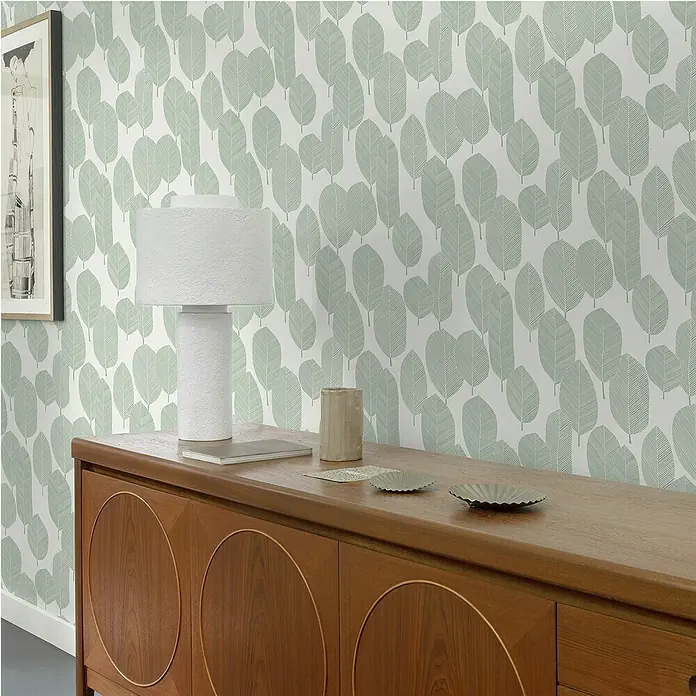 Papel pintado Vegetal Hojas Bosque - Verde, Floral, 10 x 0,53 m - Un elegante aparador de madera con detalles redondos, decorado con una lámpara, posavasos y un pequeño libro.