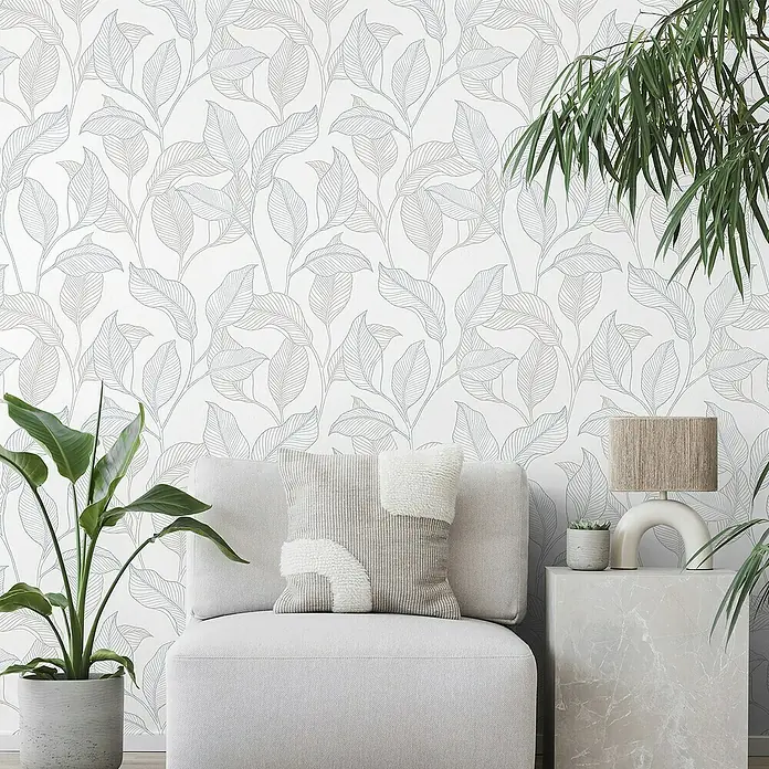 Papel pintado Vegetal Hojas - Azul, Floral, 10 x 0,53 m - Primer plano de una habitación con papel tapiz con un elegante patrón de hojas azules y marrones, un sillón de color claro, plantas y una lámpara.