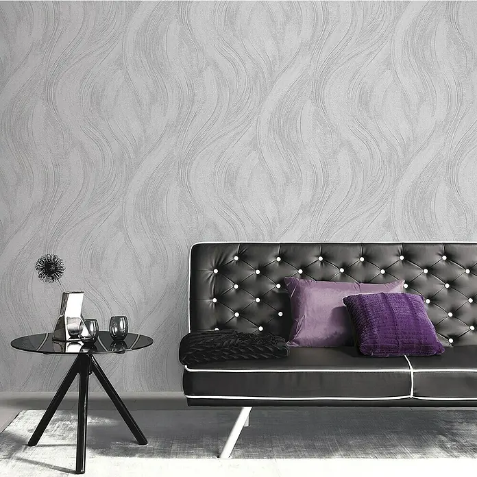 Papel pintado Texturado Ondas - Gris, Ondas, 10 x 0,53 m - Primer plano de un sofá negro elegante con cojines morados y una mesa auxiliar con decoraciones.