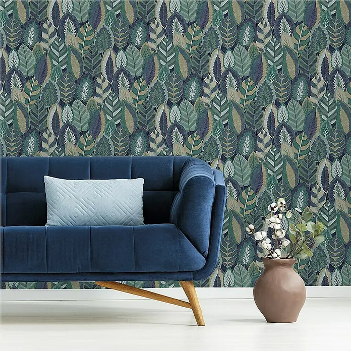 Papel pintado Hojas - Azul, Floral, 10 x 0,53 m - Un sofá de terciopelo azul marino con un cojín celeste contra una pared con un diseño de hojas, y un jarrón con ramas de algodón.