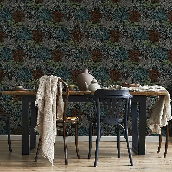 Papel pintado Botánico Palmeras - Negro, Floral, 10 x 0,53 m - Comedor atmosférico con una mesa de comedor y sillas contra un papel pintado botánico oscuro con exuberante follaje en tonos marrones, verdes y grises.