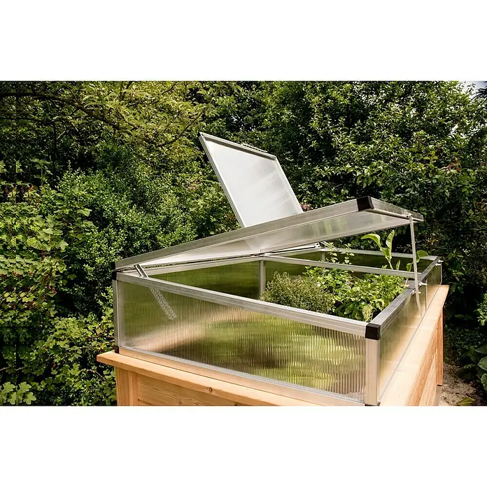 KGT Frühbeet-Aufsatz Hochbeet 210 - Passend für: KGT Hochbeet 210, L x B x H: 205 x 91 x 31 cm - Das Bild zeigt ein Mini-Gewächshaus mit geöffneten Deckeln auf einem Holztisch im Freien, umgeben von Grünpflanzen.