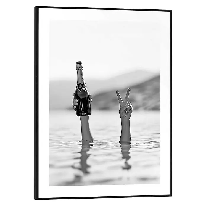Reinders Bild Slim Frame - Sea Cheers, B x H: 30 x 40 cm - Schwarz-Weiß-Foto einer Person, die eine Champagnerflasche und ein Friedenszeichen im Wasser hält, mit Bergen im Hintergrund.
