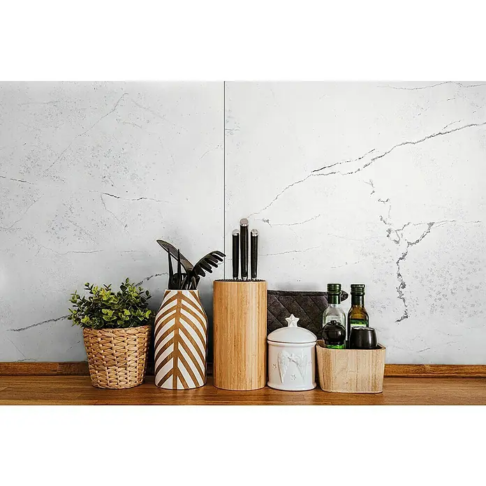 LOGOCLIC Wandpaneel Designwall - Carrara, 265 x 123 cm - Küchenutensilien-Arrangement mit Messern, Behältern und Pflanzen auf einer hölzernen Arbeitsplatte vor einer Marmorwand.