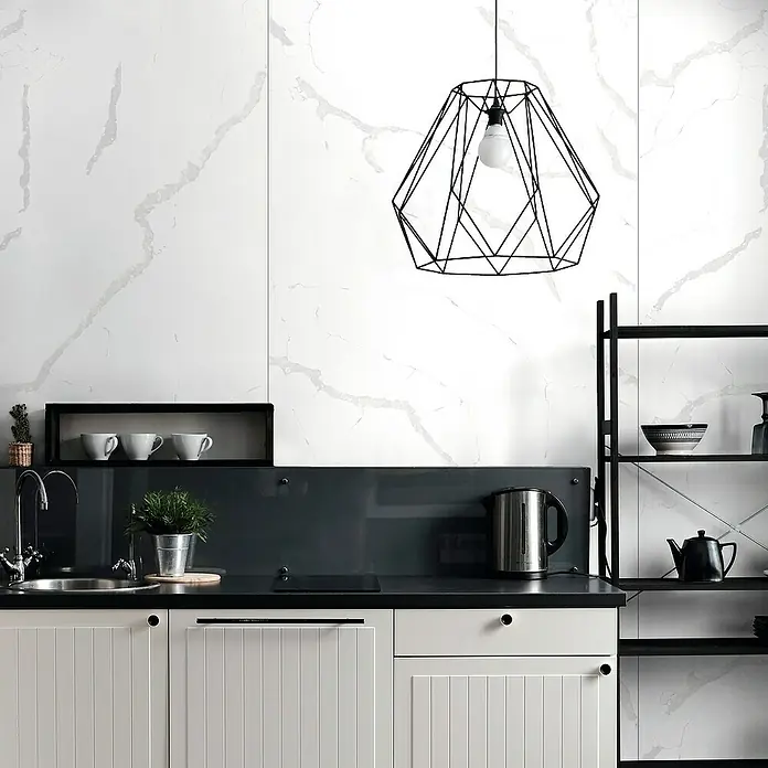 LOGOCLIC Wandpaneel Designwall - Statuario Bianco, 265 x 123 cm - Eine moderne Küche mit weißen Schrankfronten, einer dunklen Arbeitsplatte und einer markanten, geometrischen Pendelleuchte, die den Raum stilvoll beleuchtet.