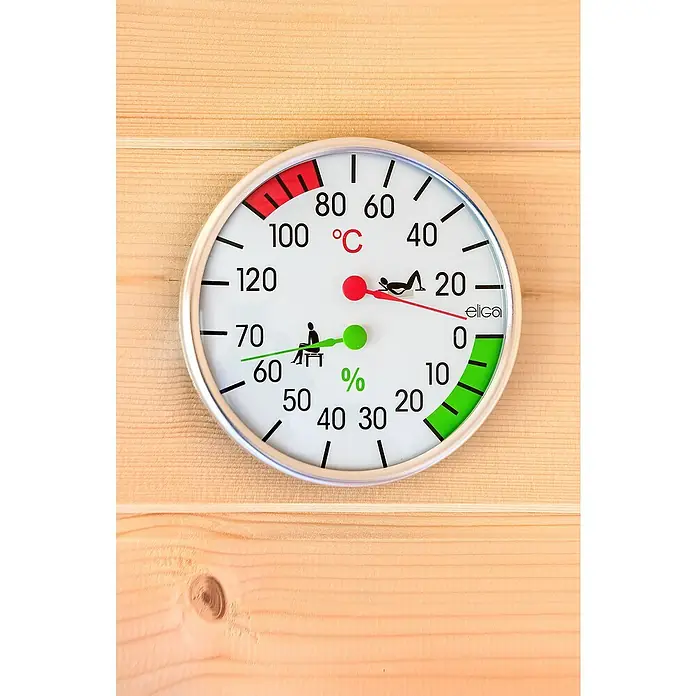 Tuindeco Aufguss-Set - Holz - Nahaufnahme eines runden Sauna-Thermo-Hygrometers mit silbernem Rahmen auf Holz, das Temperatur und Luftfeuchtigkeit anzeigt.