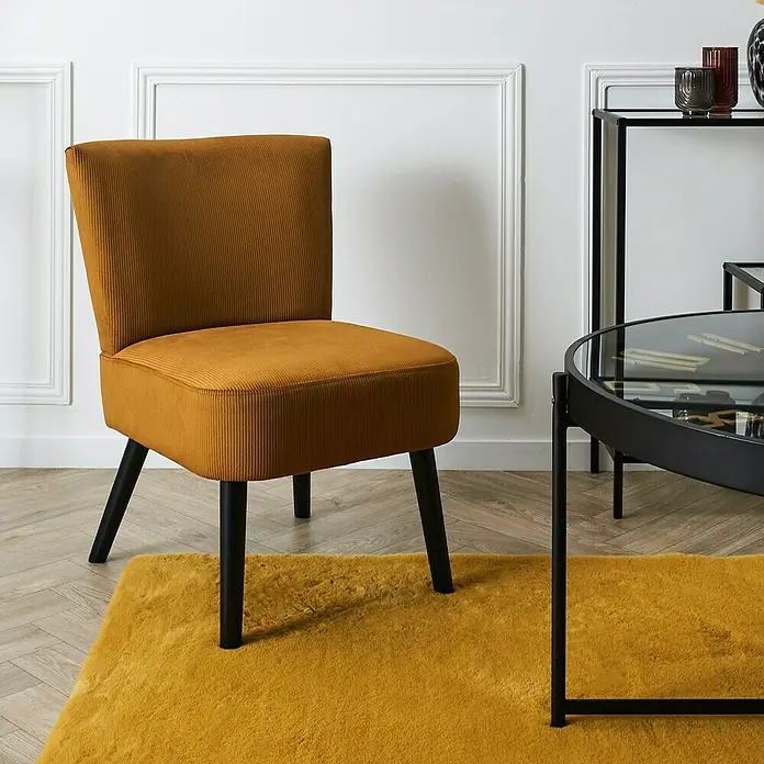 Home Deco Factory Giulia Silla - L x An x Al: 55 x 68 x 76 cm, Mostaza - Elegante sillón de pana dorada con patas negras sobre una alfombra a juego. Un mueble moderno que combina estilo y comodidad.