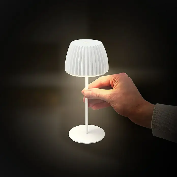 Brilo Riffle Akku-Tischleuchte - Ø x H: 8,5 x 20,1 cm, Weiß, Warmweiß, 1,5 W, IP44, Mini - Nahaufnahme einer weißen Tischleuchte mit Lampenschirm, die von einer Hand gehalten wird.
