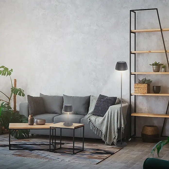 Brilo Riffle Akku-Stehleuchte Maxi - Ø x H: 19 x 124,1 cm, Anthrazit, Warmweiß, 4,2 W, IP44 - Modernes Wohnzimmer mit grauer Couch, Holztisch und einer dekorativen Tischleuchte sowie Stehlampe mit grauem Schirm.