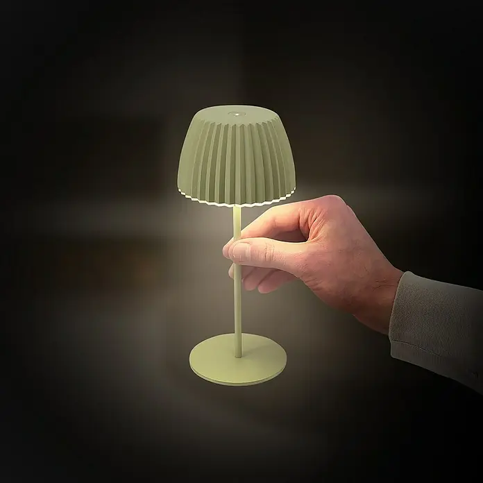 Brilo Riffle Akku-Tischleuchte - Ø x H: 8,5 x 20,1 cm, Grün, Warmweiß, 1,5 W, IP44, Mini - Eine Hand hält eine stilvolle, grüne Tischleuchte, die ein warmes Licht ausstrahlt und eine gemütliche Atmosphäre schafft.