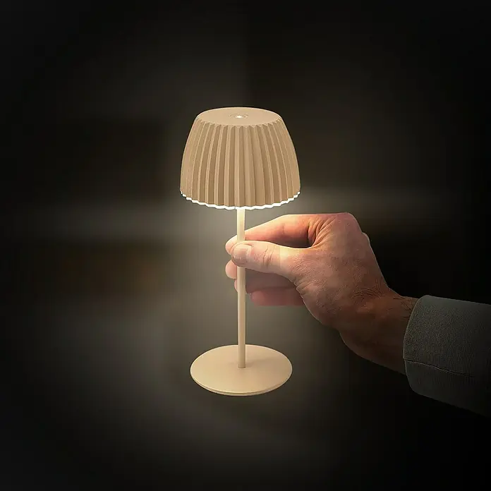 Brilo Riffle Akku-Tischleuchte - Ø x H: 8,5 x 20,1 cm, Beige, Warmweiß, 1,5 W, IP44, Mini - Nahaufnahme einer beigen Tischleuchte, die von einer Hand gehalten wird. Elegantes Design für eine gemütliche Atmosphäre.