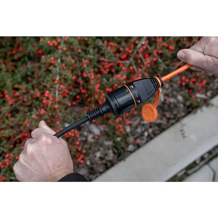 UniTEC Verlängerungskabel mit arretierbarer Kupplung - 20 m, Orange, IP44, H07BQ - Verlängerungskabel mit wasserdichter Kupplung in Händen. Das orangefarbene Kabel ist mit einer schwarzen Kupplung verbunden.