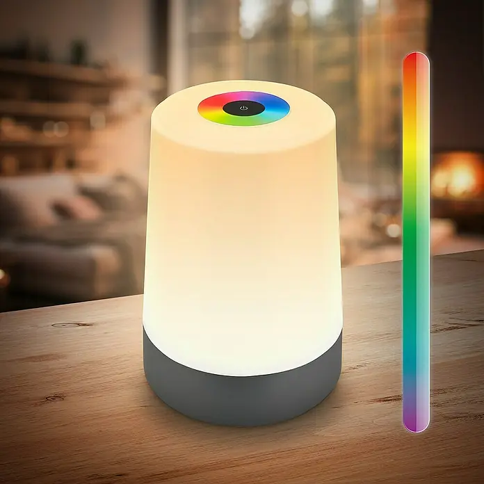 Brilo Akku-Tischleuchte Nubsi - Ø x H: 9 x 13 cm, Antharzit, RGBW, 2,8 W, IP44 - Nahaufnahme einer farbwechselnden Nachttischlampe mit einem Farbspektrum daneben auf einem Holztisch, die eine gemütliche Atmosphäre erzeugt.