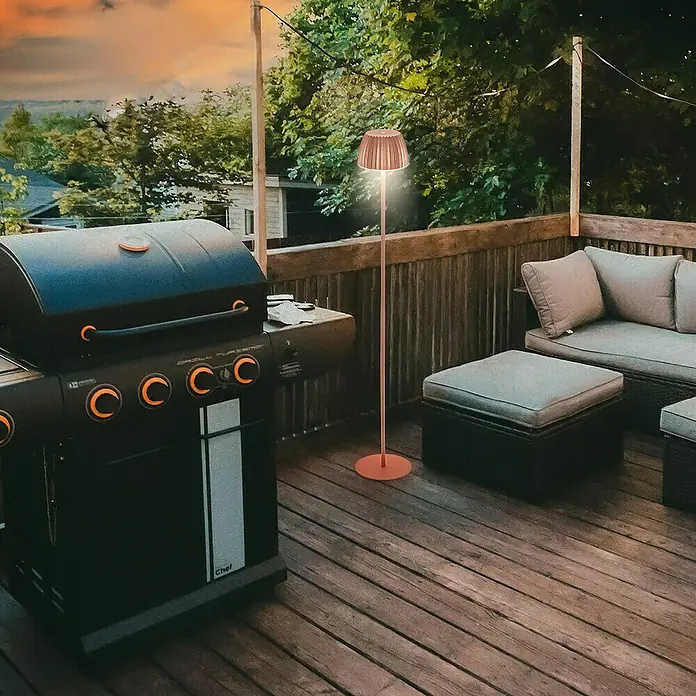 Brilo Riffle Akku-Stehleuchte Maxi - Ø x H: 19 x 124,1 cm, Kupfer, Warmweiß, 4,2 W, IP44 - Outdoor-Szene mit einem Grill und einer eleganten Stehlampe, die eine warme Atmosphäre auf der Holzterrasse erzeugt.