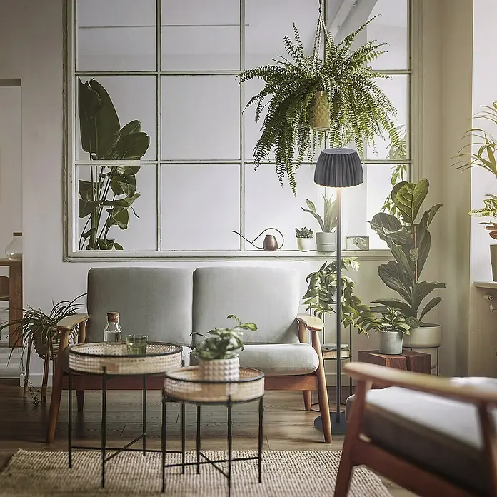 Brilo Riffle Akku-Stehleuchte Maxi - Ø x H: 19 x 124,1 cm, Anthrazit, Warmweiß, 4,2 W, IP44 - Wohnzimmer mit grauem Sofa, Beistelltischen und einer eleganten Stehlampe, die das Ambiente stilvoll beleuchtet. Viele Pflanzen im Raum.