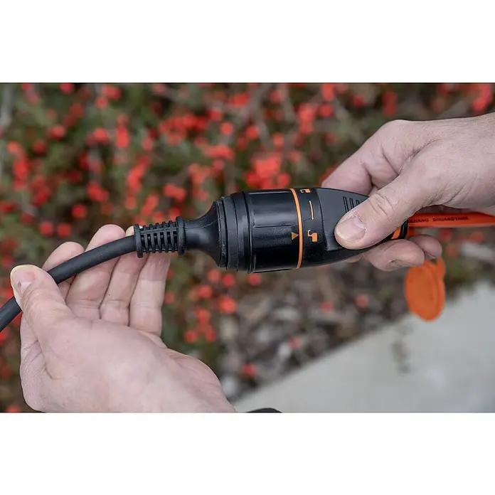 UniTEC Verlängerungskabel mit arretierbarer Kupplung - 20 m, Orange, IP44, H07BQ - Ein schwarzes Verlängerungskabel mit einem orangefarbenen Drehmechanismus wird von zwei Händen gehalten.