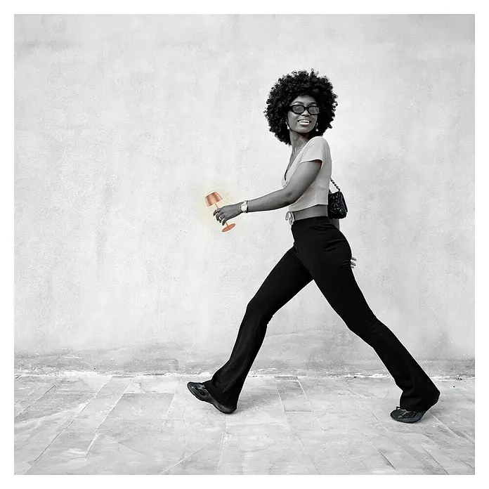 Brilo Riffle Akku-Tischleuchte - Ø x H: 8,5 x 20,1 cm, Kupfer, Warmweiß, 1,5 W, IP44, Mini - Eine stilvolle Frau mit Afro, Sonnenbrille und schwarzer Schlaghose spaziert mit einer modernen, goldenen Tischleuchte in der Hand.