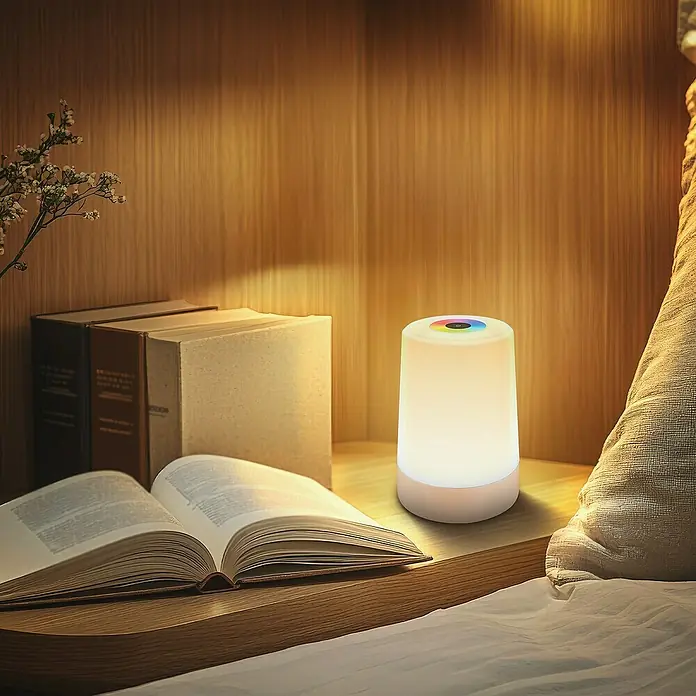 Brilo Akku-Tischleuchte Nubsi - Ø x H: 9 x 13 cm, Beige, RGBW, 2,8 W, IP44 - Stimmungsvolle Aufnahme einer Nachttischlampe, die warmes Licht spendet, neben einem aufgeschlagenen Buch und dekorativen Elementen.