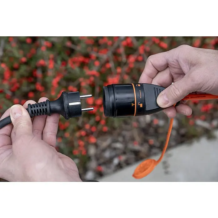 UniTEC Verlängerungskabel mit arretierbarer Kupplung - 20 m, Orange, IP44, H07BQ - Nahaufnahme eines Steckers, der in eine Verlängerung gesteckt wird, vor einem Hintergrund von roten Beeren.