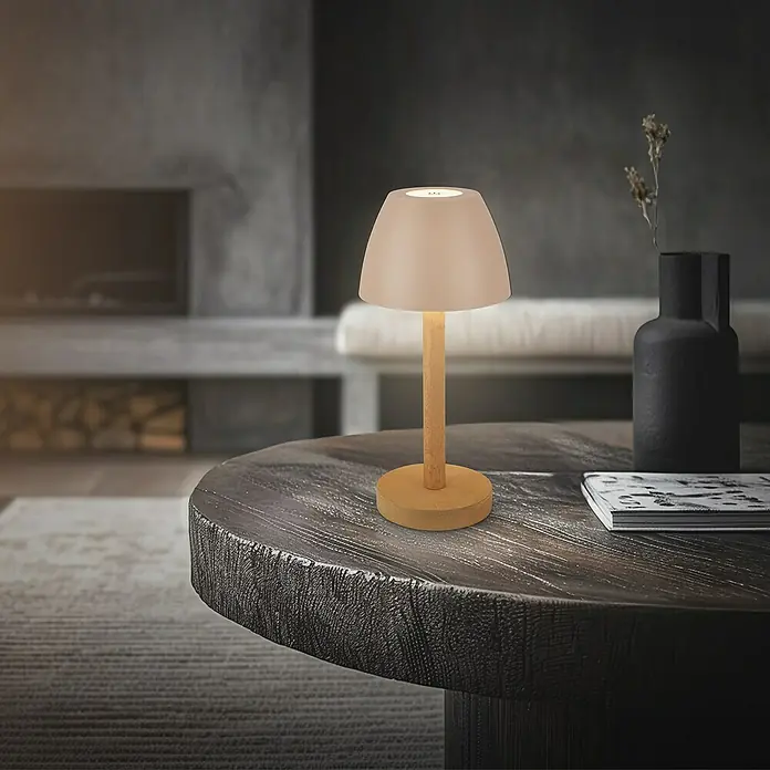 Brilo Akku-Tischleuchte Serina Wood - Ø x H: 13,5 x 20 cm, Beige, Warmweiß, 2,5 W, IP44 - Nahaufnahme einer Tischleuchte mit Holzfuß und sanftem Licht auf einem runden Tisch.