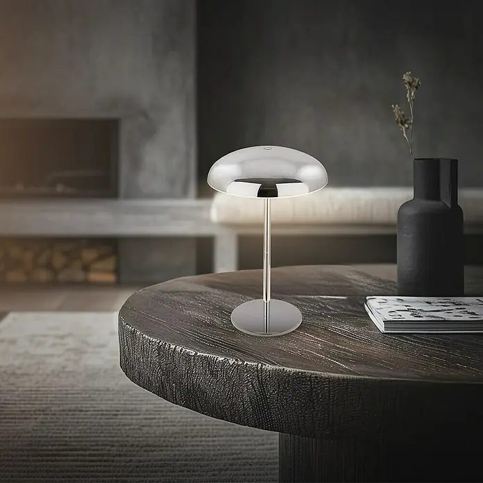 Brilo Akku-Tischleuchte Caxa - Ø x H: 19,5 x 30,5 cm, Chrom, Warmweiß, 2,8 W, IP44 - Stilvolle silberne Tischleuchte auf einem dunklen Holztisch, ergänzt das moderne Wohnambiente mit sanftem Licht.