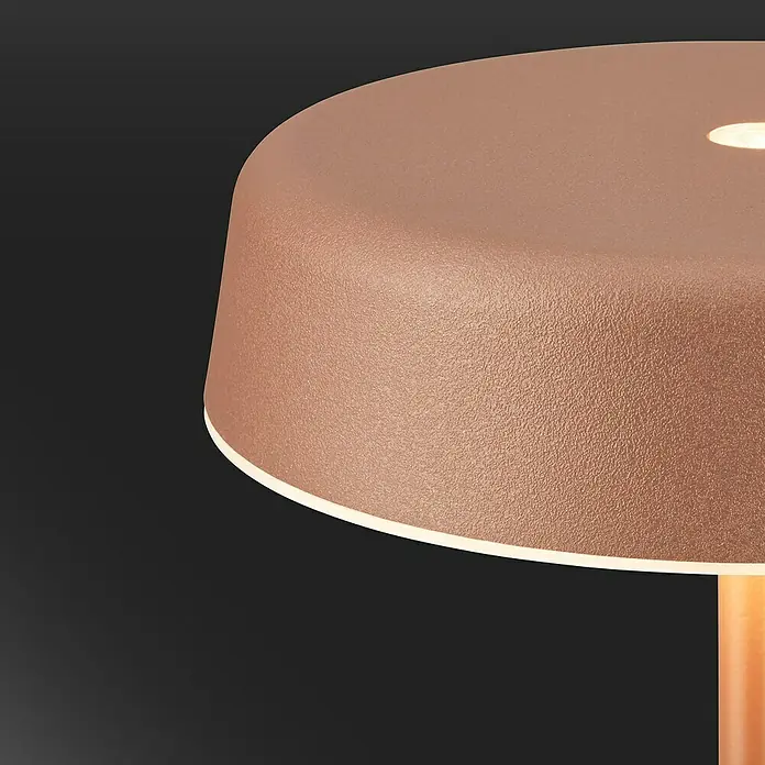 Brilo Akku-Tischleuchte Pala - Ø x H: 13 x 36,5 cm, Coffee, Warmweiß, 2,6 W, IP44 - Nahaufnahme einer modernen kupferfarbenen Tischleuchte mit einem warmen Lichtschein und einer strukturierten Oberfläche.