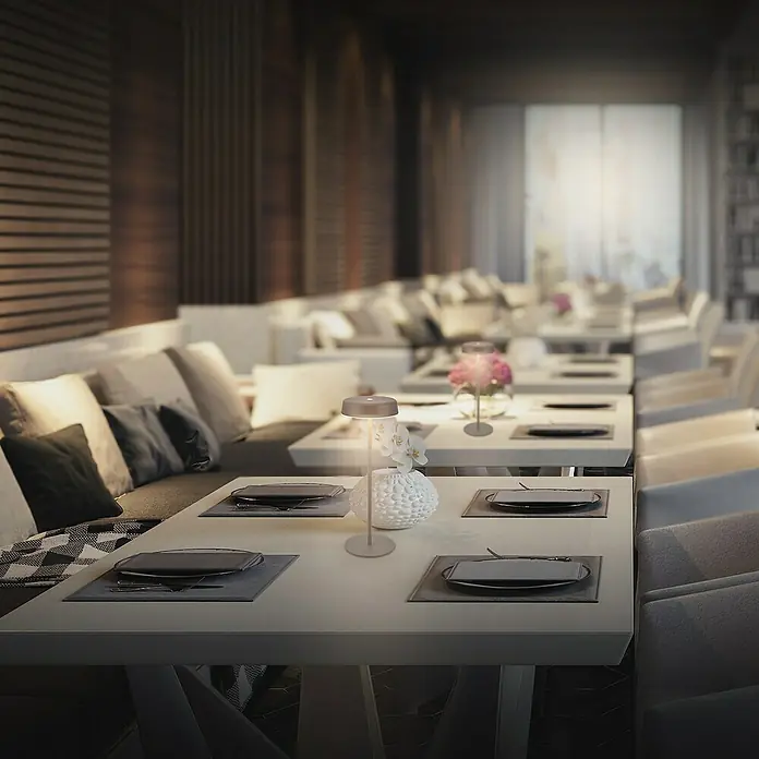 Brilo Akku-Tischleuchte Pala - Ø x H: 13 x 36,5 cm, Anthrazit, Warmweiß, 2,6 W, IP44 - Elegante Tischleuchte auf einem gedeckten Tisch in einem stilvollen Restaurant. Die Lampe spendet warmes Licht und sorgt für eine angenehme Atmosphäre.