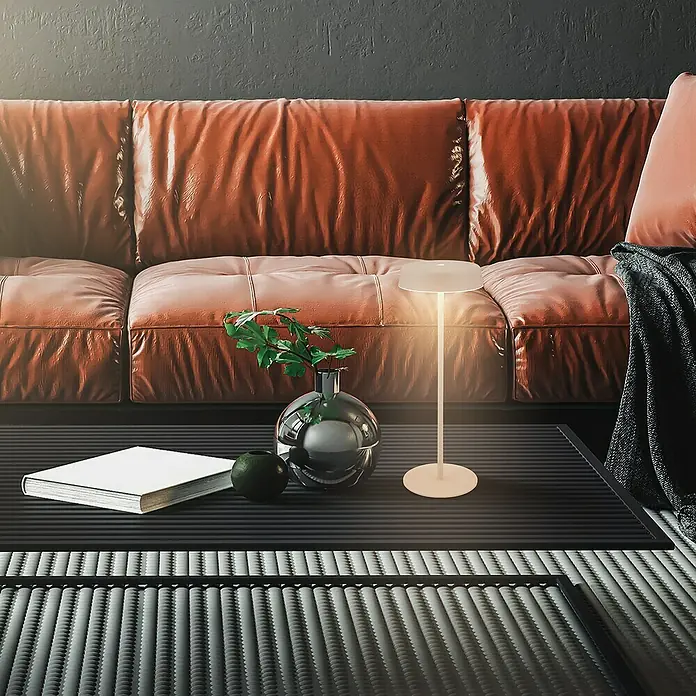 Brilo Akku-Tischleuchte Pala - Ø x H: 13 x 36,5 cm, Beige, Warmweiß, 2,6 W, IP44 - Nahaufnahme einer stilvollen Tischlampe auf einem Couchtisch mit Buch und Dekoration, vor einem Ledersofa.