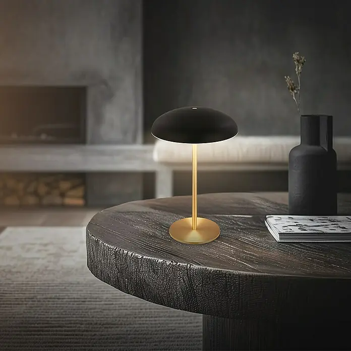 Brilo Akku-Tischleuchte Caxa - Ø x H: 19,5 x 30,5 cm, Schwarz, Warmweiß, 2,8 W, IP44 - Elegante Tischleuchte in Schwarz und Gold auf einem Holztisch. Die Lampe spendet warmes Licht und sorgt für eine gemütliche Atmosphäre.