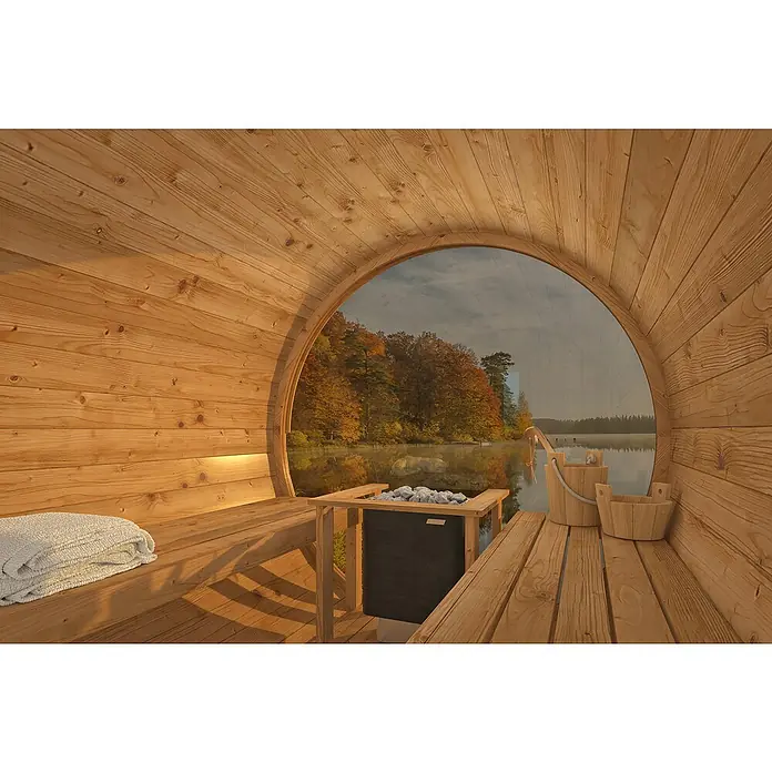 Tuindeco Fasssauna - L x B x H: 300 x 205 x 220 cm, Ohne Ofen, Großes Panoramafenster - Ein Fass-Sauna-Innenraum mit Holzbänken, Handtuch, Saunaofen und Blick auf einen ruhigen See mit Bäumen im Herbst.