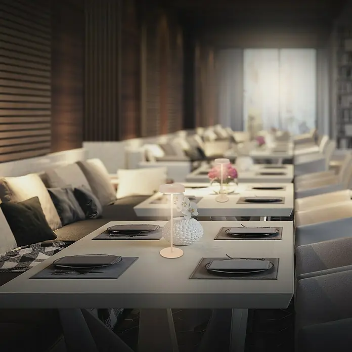 Brilo Akku-Tischleuchte Pala - Ø x H: 13 x 36,5 cm, Beige, Warmweiß, 2,6 W, IP44 - Elegante Tischleuchte auf einem gedeckten Tisch in einem stilvollen Restaurant, die eine warme und einladende Atmosphäre schafft.