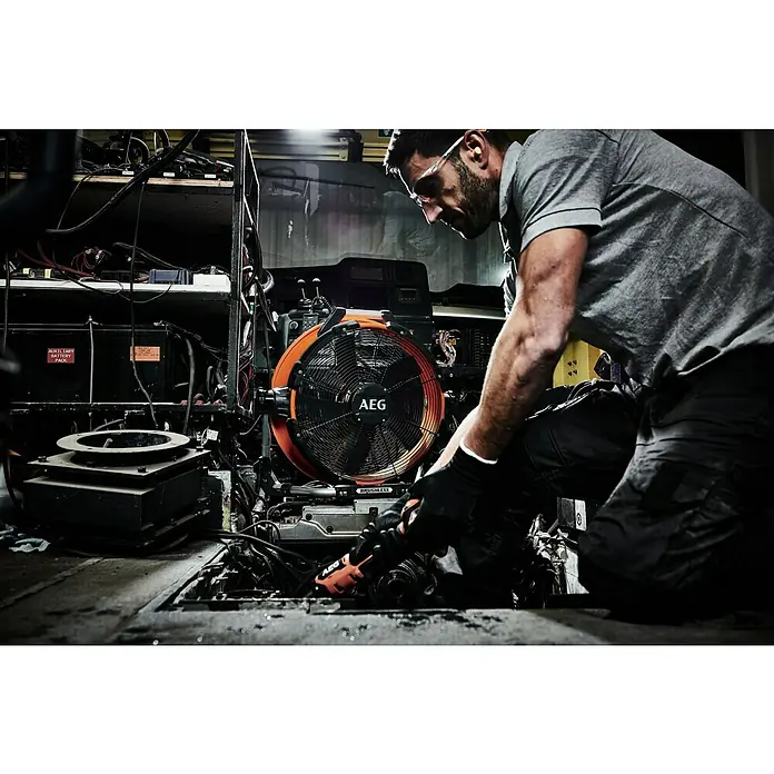 AEG Pro 18V Hybrid-Ventilator BDF18-0 - 18 V, Ohne Akku, Schwenkbereich: 210 ° - Ein Handwerker repariert eine Maschine mit Werkzeug von AEG. Ein großer Ventilator der Marke AEG steht daneben zur Kühlung.