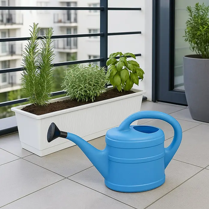Geli Gießkanne - Hellblau, 2 l - Eine blaue Gießkanne steht auf einem Balkon neben einem Blumenkasten mit verschiedenen Kräutern, darunter Rosmarin und Basilikum.