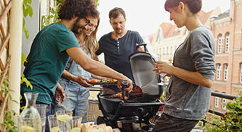 Mehrere Personen stehen am Balkon und grillen am kleinen Elektrogrill