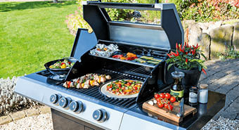 Gasgrill im Garten mit verschiedenen Speisen beladen