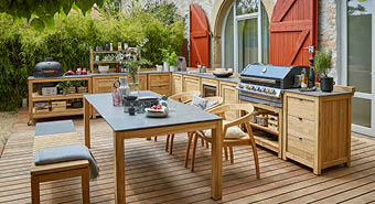 Terrasse mit Gartentisch und Sesseln, dahinter eine große Grillküche in L-Form mit Griller