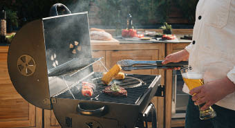 Mann grillt am Holzkohlegrill Fleisch und Mais