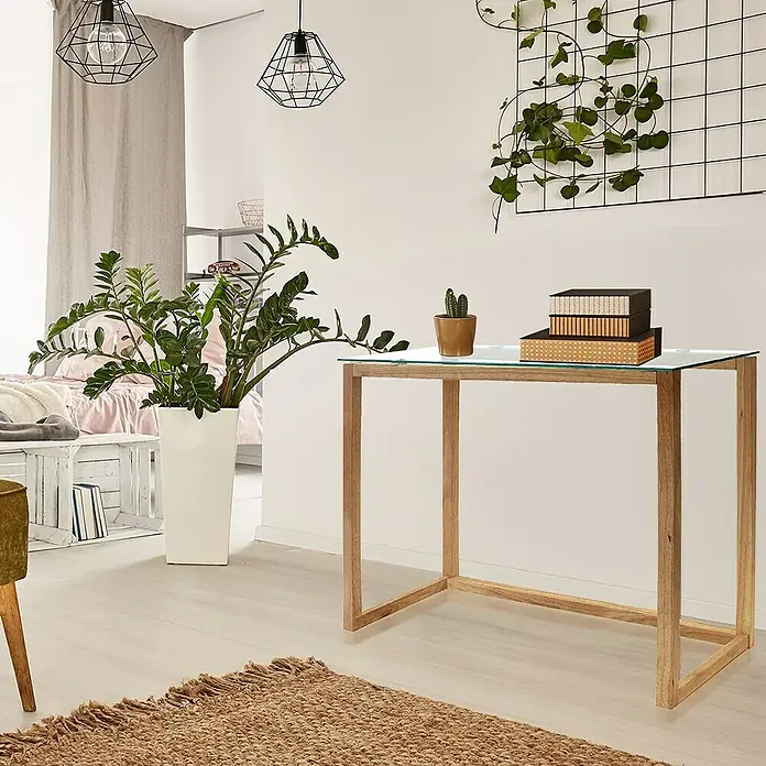 Home Deco Factory Mesa auxiliar - L x An x Al: 32 x 100 x 87 cm, Vidrio templado/Madera de hevea - Un escritorio moderno con una tapa de vidrio y marco de madera, adornado con plantas y libros, que añade un toque de estilo a cualquier habitación.