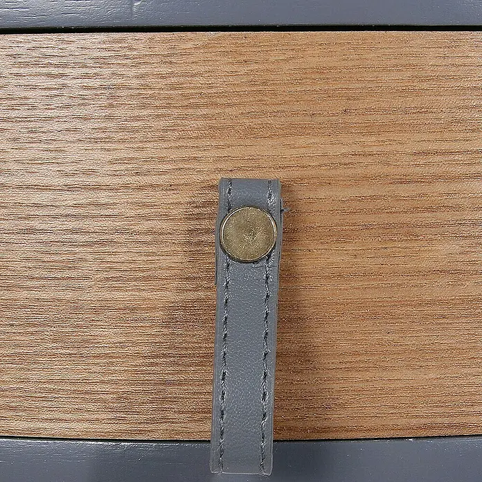 Home Deco Factory Mesa auxiliar - Ø x Al: 35 x 46,5 cm, Gris/Madera, Número de cajones: 1 ud. - Primer plano de un cajón con tirador de cuero gris y botón dorado, parte de un mueble.