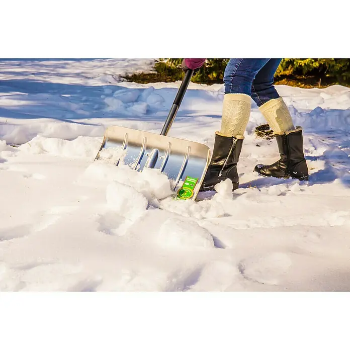 Freund Victoria Schneeschieber Profi - Breite: 50 cm, Langstiel, Material Stiel: Aluminium - Eine Person schaufelt Schnee mit einer Schneeschaufel, wobei ein grünes Produktpaket im Schnee liegt.