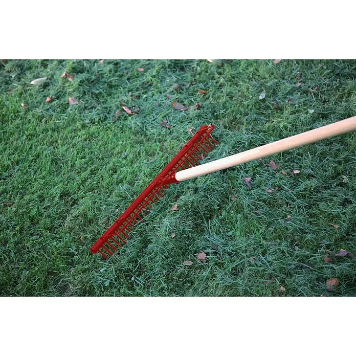 Gardol Rasenrechen - Arbeitsbreite: 58,5 cm, Anzahl Zinken: 32, Langstiel - Ein roter Rechen mit Holzstiel liegt auf grünem Gras. Gartenarbeit leicht gemacht mit diesem robusten Rechen!
