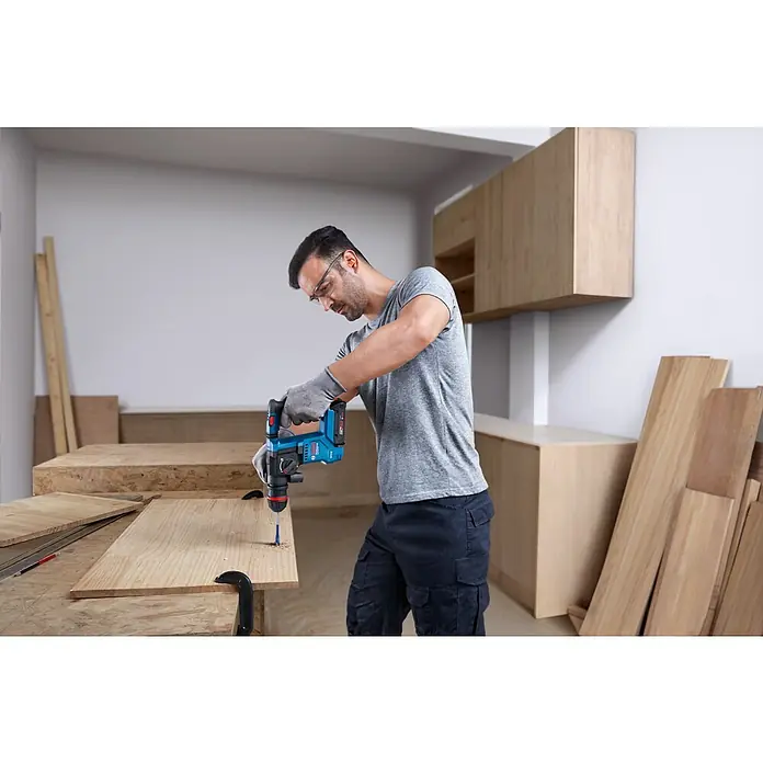 Bosch Professional AMPShare 18V Juego de máquinas - 18 V, 1 batería, 2 Ah, 4 pzs. - Un manitas usa un taladro azul Bosch para hacer un agujero en una tabla de madera. El taladro es inalámbrico y potente.