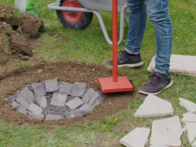 Mit einem Betonstampfer wird ein Ring rund um die Feuerstelle eben gestampft