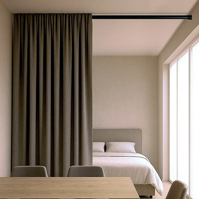 Barra para cortinas extensible multiusos - Metal, Negro, Longitud regulable: 140 cm - 250 cm - Habitación amueblada con una cortina negra colgada de una barra negra, dividiendo el espacio en dos zonas separadas.