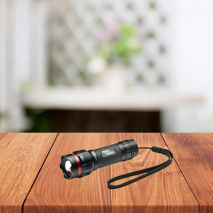 Profi Depot Linterna KE120 - 120 lm, IP44 - Una linterna LED táctica negra con correa de mano reposa sobre una mesa de madera, lista para usar.